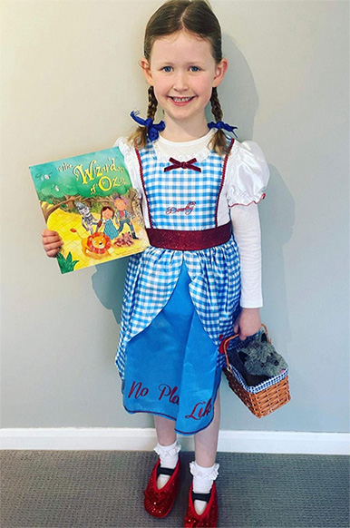 Child wearing fancy dress outfit whilst holding Wizard of Oz book.