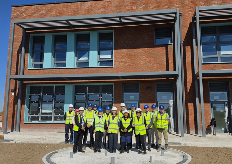 A group of people in high visibility vests and hard hats pose in front of Kings Moat Community Primary School
