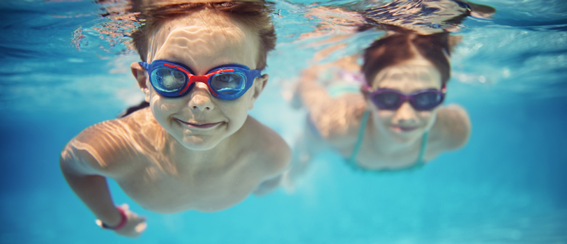 Two children swimming under water wearing water goggles.