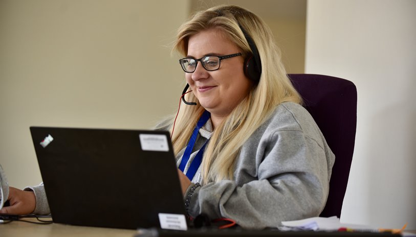 A woman using a headset sat in front of a laptop.