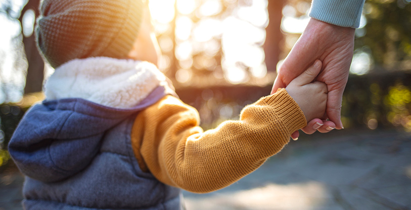 Close up of mother and a child hands at the sunset. A parent holds the hand of a small boy in the sunset. Mother holding her little boys hand walking down the street