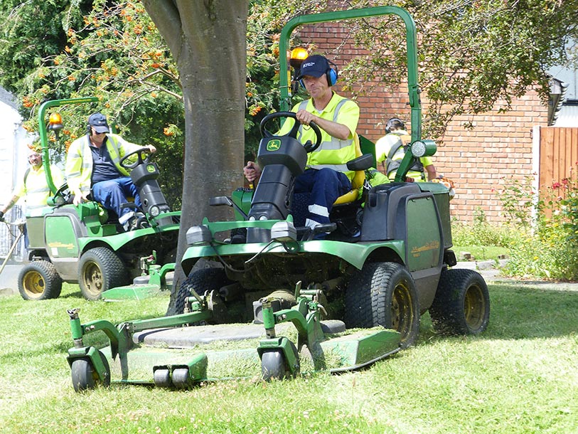 Grounds maintenance worker cutting grass with a ride-on mower in a UK public park