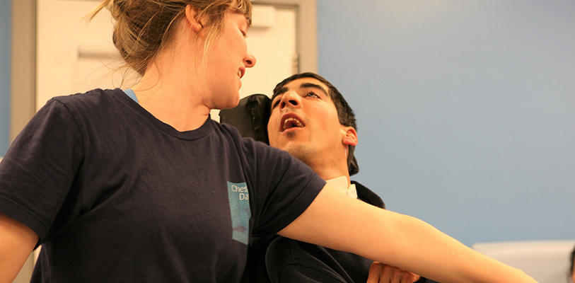 A care worker supporting a seated person in a specialist chair during an assisted movement activity