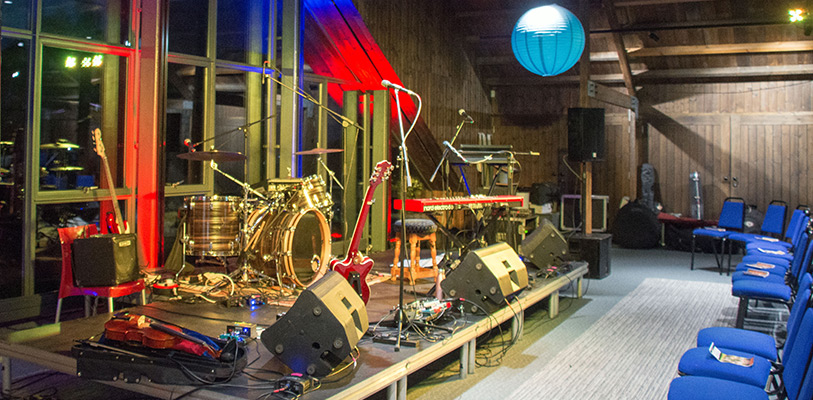 Stage with musical instruments and equipment along with blue chairs for audience seating.