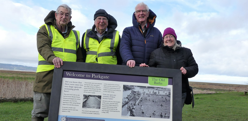 Members of the Parkgate Society stood by the marsh waterfront with the board that will be situated at the Old Baths.
