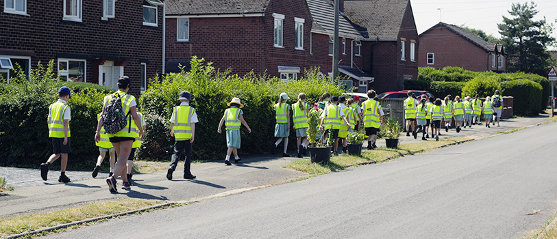 School pupils and teachers walking in hi-vis jackets along residential pavements