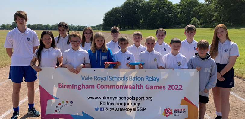 Young people and children stood on a running track holding batons and a sign.