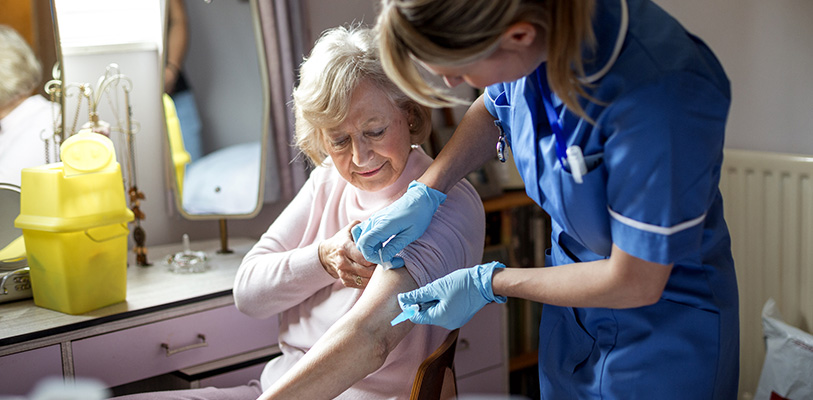 A nurse visits an elderly woman in her home. The elderly woman is happily sitting on a chair at her dressing table.