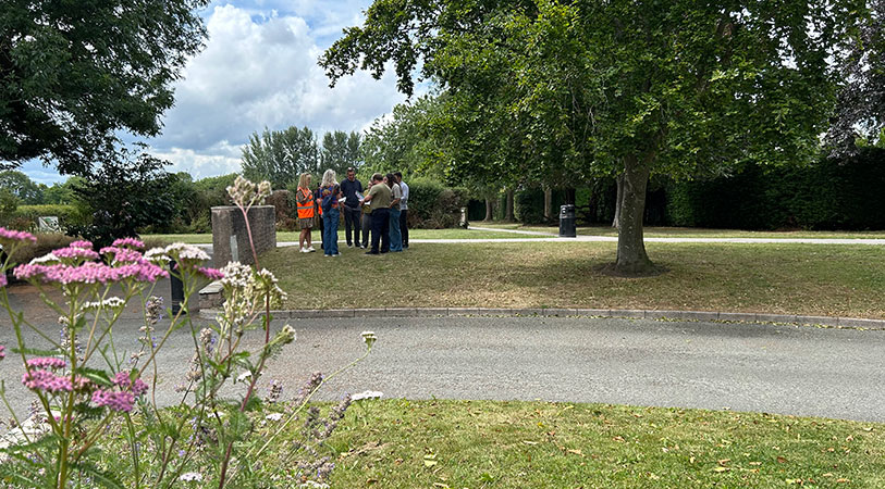 Group of walkers talking in the park, surrounded by trees, as well as pink and white flowers.