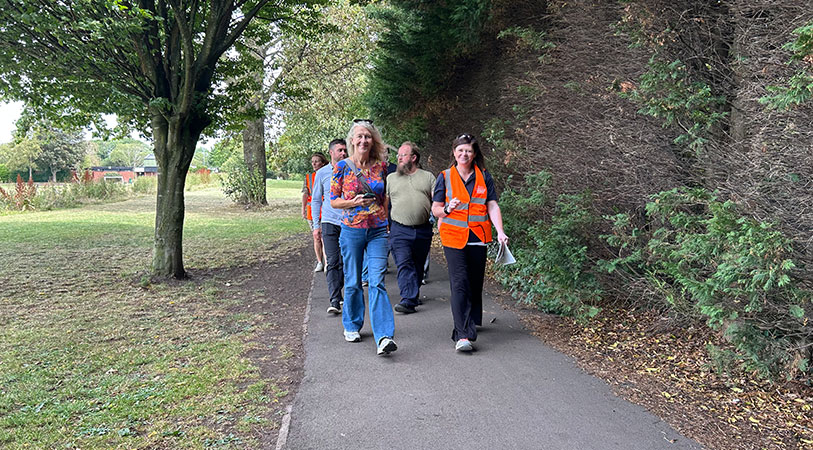 Cllr Gittins and council staff walking along a path in park surrounded by trees, grass and bushes.