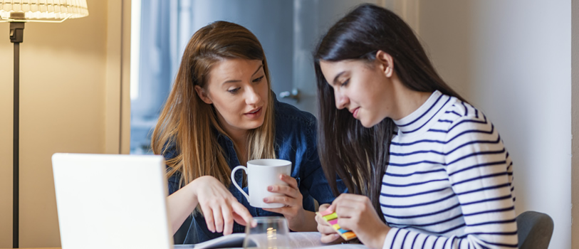 Two people organising in front of a computer with a drink.