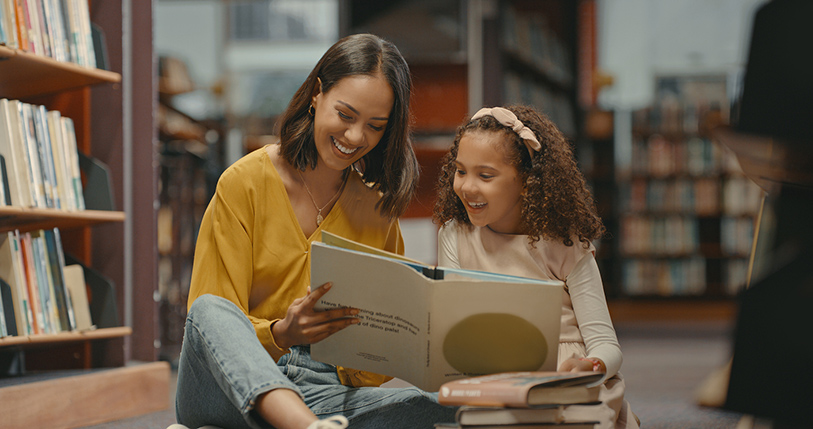 Two females reading a book together in a library.
