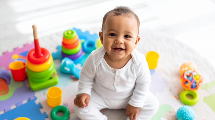 Baby sat smiling surrounded by toys