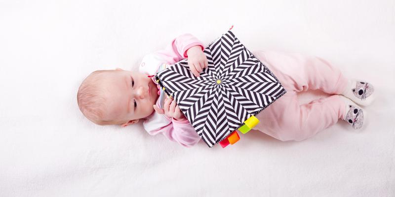 A baby lying on a blanket holding a sensory toy