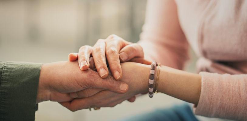 Young person holds elderly hand.