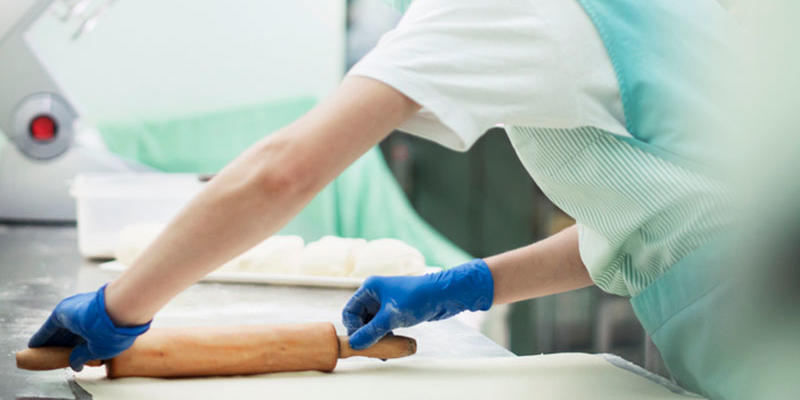Baker rolling out pastry wearing hair net, mask and gloves.