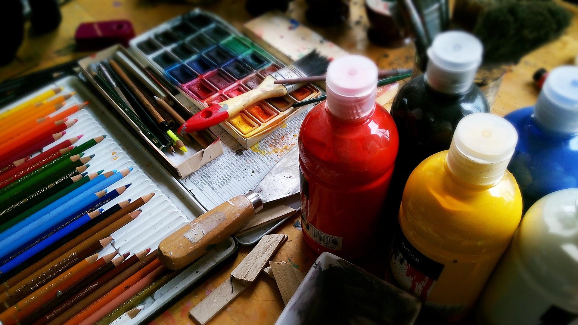 a pile of art materials including paints, pencils and paintbrushes