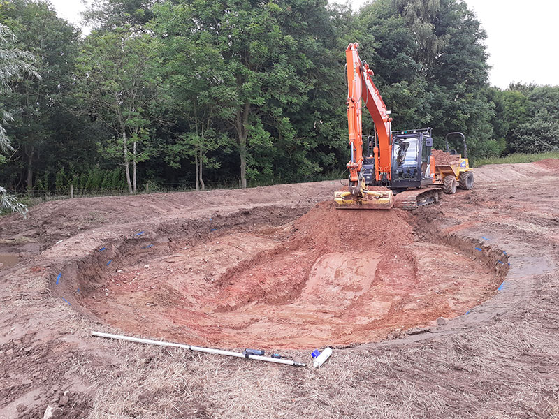 Mechanical digger lifting soil to create a circular pond