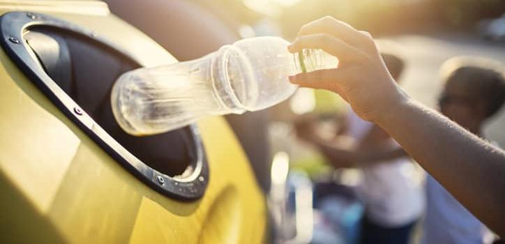 Plastic bottle being thrown in recycling bin.