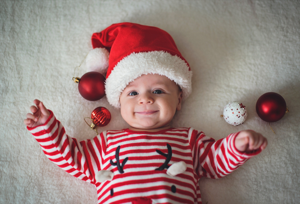 A baby lying down with a Santa hat on their head.
